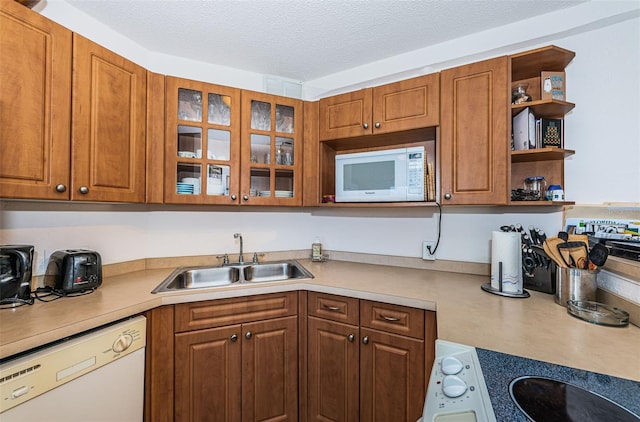 kitchen with brown cabinetry, open shelves, a sink, light countertops, and white appliances