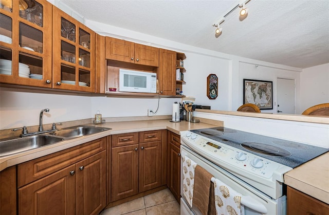 kitchen with white appliances, glass insert cabinets, light countertops, a textured ceiling, and a sink