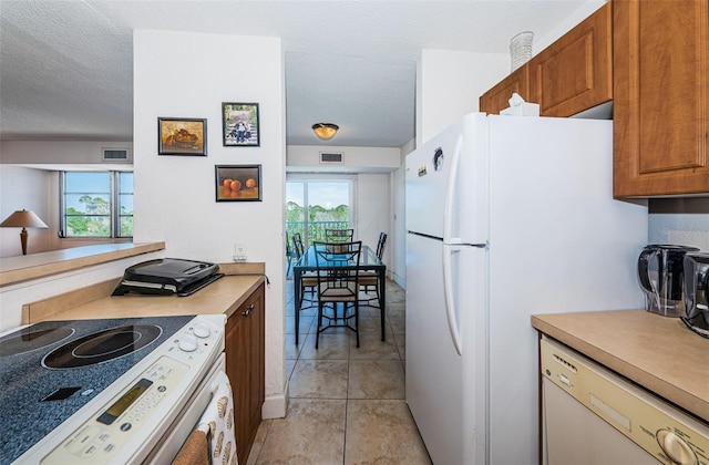 kitchen with brown cabinets, white appliances, a textured ceiling, light tile patterned floors, and visible vents
