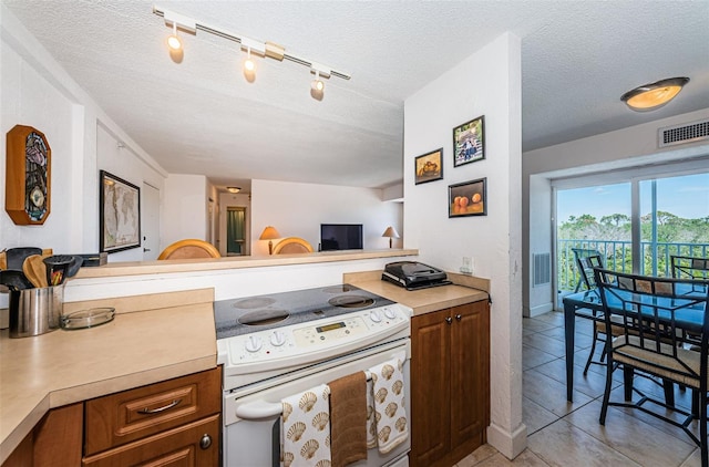 kitchen featuring light countertops, white range with electric cooktop, a textured ceiling, brown cabinetry, and visible vents