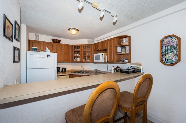 kitchen featuring a textured ceiling, a sink, a peninsula, glass insert cabinets, and white appliances