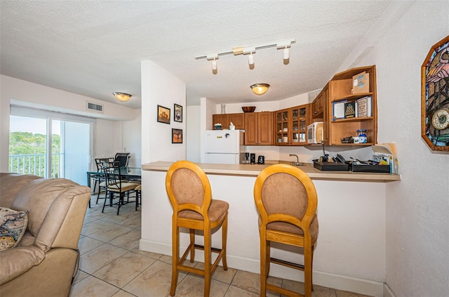 kitchen featuring white appliances, brown cabinets, a textured ceiling, and glass insert cabinets