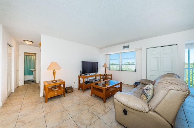 living room featuring a textured ceiling, visible vents, plenty of natural light, and light tile patterned floors