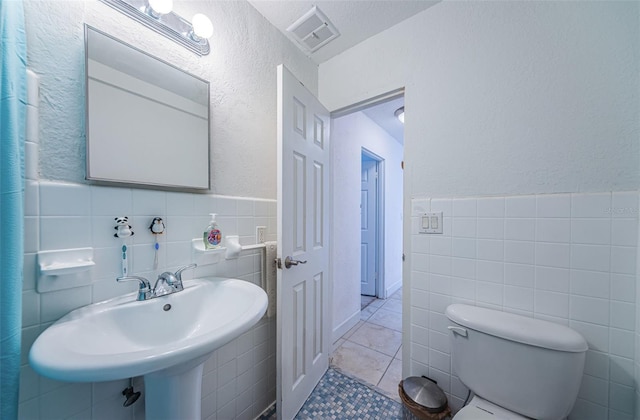 bathroom with tile walls, a textured wall, tile patterned floors, and visible vents
