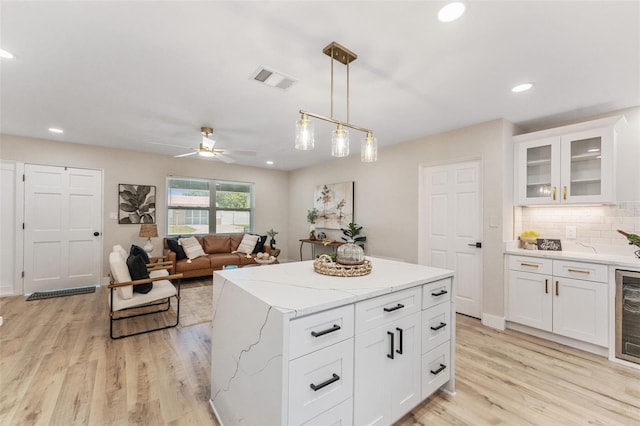 7494 7th St N, Saint Petersburg, FL 33702 - kitchen featuring hanging light fixtures, tasteful backsplash, light stone countertops, light wood finished floors, and white cabinetry