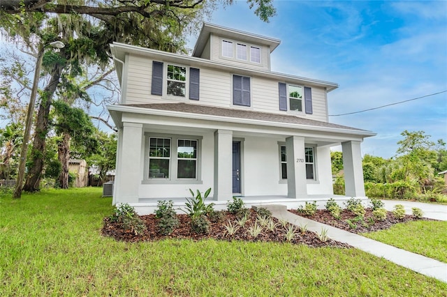 american foursquare style home featuring covered porch, a shingled roof, and a front yard