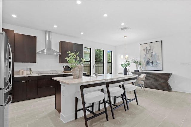 kitchen with a sink, wall chimney range hood, a breakfast bar, stainless steel refrigerator with ice dispenser, and visible vents