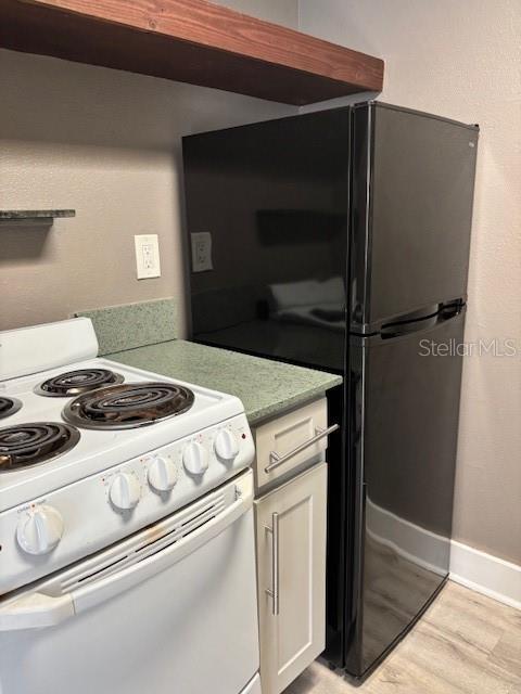 4127 Dolphin Dr Unit 4127, Tampa, FL 33617 - kitchen featuring white cabinets, white range with electric stovetop, light wood-style floors, light countertops, and freestanding refrigerator