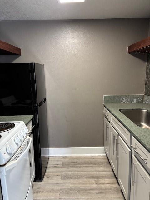4127 Dolphin Dr Unit 4127, Tampa, FL 33617 - kitchen featuring dark countertops, a sink, light wood finished floors, baseboards, and white stove