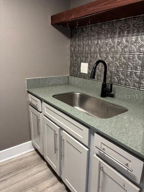 4127 Dolphin Dr Unit 4127, Tampa, FL 33617 - kitchen featuring decorative backsplash, a sink, stone countertops, light wood-style floors, and white cabinetry