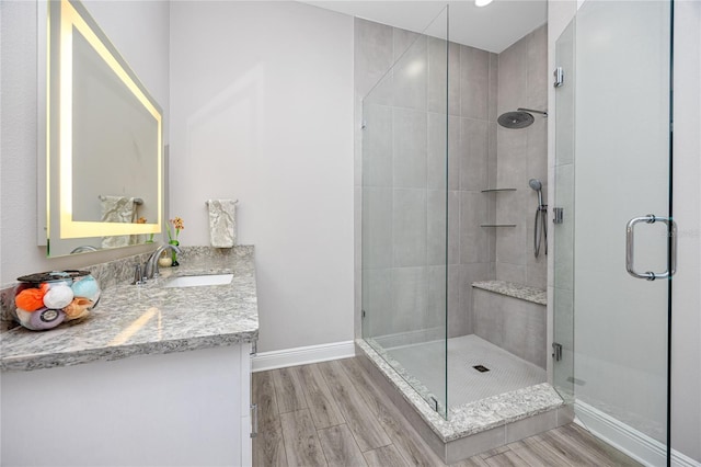 full bath featuring wood finished floors, a shower stall, vanity, and baseboards