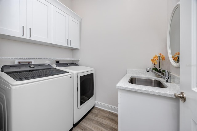laundry room featuring washer and clothes dryer, cabinet space, baseboards, and light wood-style flooring