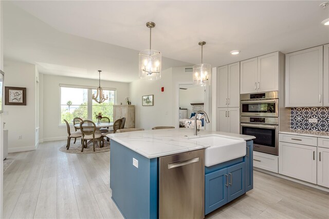 kitchen with decorative backsplash, a chandelier, stainless steel appliances, a sink, and blue cabinetry
