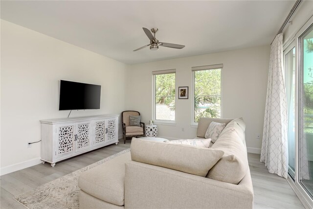 living area with baseboards, a ceiling fan, and light wood finished floors