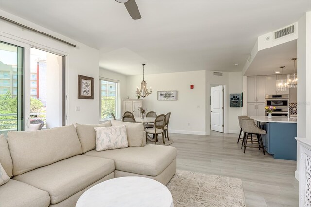 living room with visible vents, baseboards, ceiling fan with notable chandelier, and light wood-type flooring