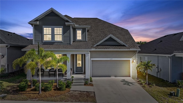 traditional-style house featuring a shingled roof, a garage, stucco siding, covered porch, and driveway