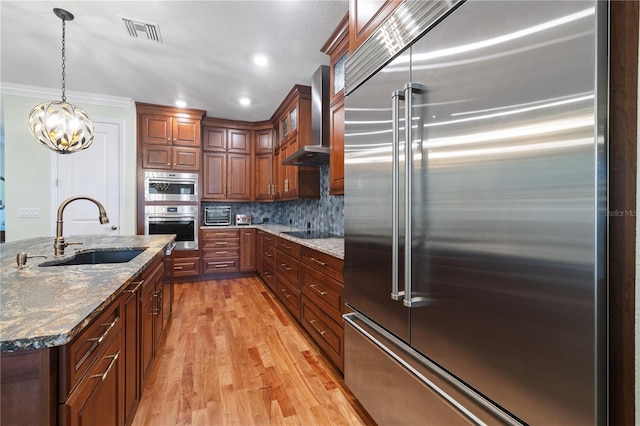 1432 Gopher Loop, Tarpon Springs, FL 34689 - kitchen with appliances with stainless steel finishes, a sink, wall chimney range hood, light wood finished floors, and dark stone counters