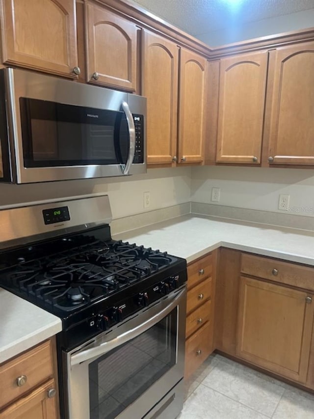 kitchen with light countertops, appliances with stainless steel finishes, light tile patterned floors, and brown cabinets