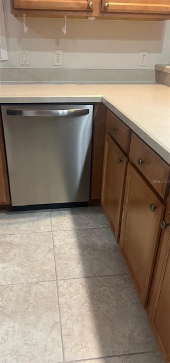 kitchen with stainless steel dishwasher, light countertops, and brown cabinetry