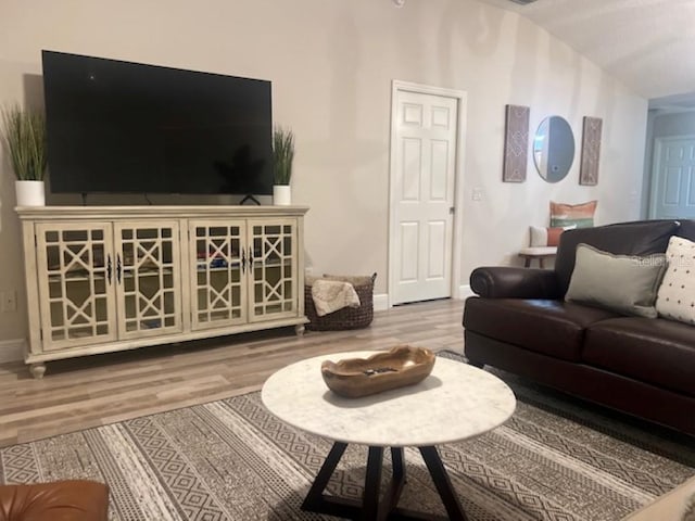 living room featuring baseboards, wood finished floors, and lofted ceiling