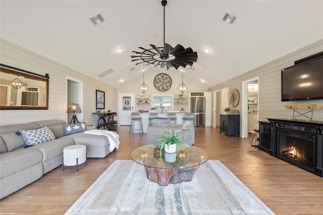 living room featuring ceiling fan, wood walls, wood finished floors, and visible vents