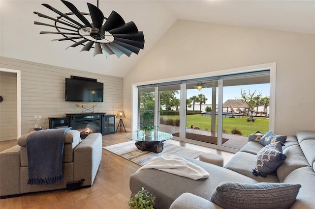 living area with a glass covered fireplace, high vaulted ceiling, ceiling fan, and light wood-type flooring