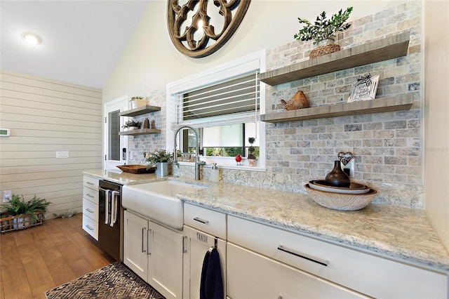 kitchen with open shelves, light stone counters, a sink, light wood-style flooring, and dishwasher