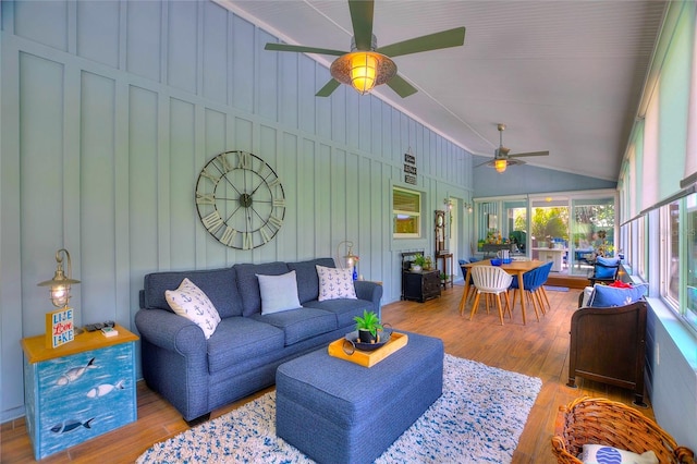 living room featuring ceiling fan, wood finished floors, vaulted ceiling, and a decorative wall