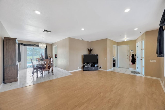 living area featuring baseboards, light wood-type flooring, a chandelier, and visible vents