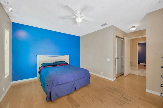 bedroom featuring a ceiling fan, a textured ceiling, visible vents, wood finished floors, and baseboards