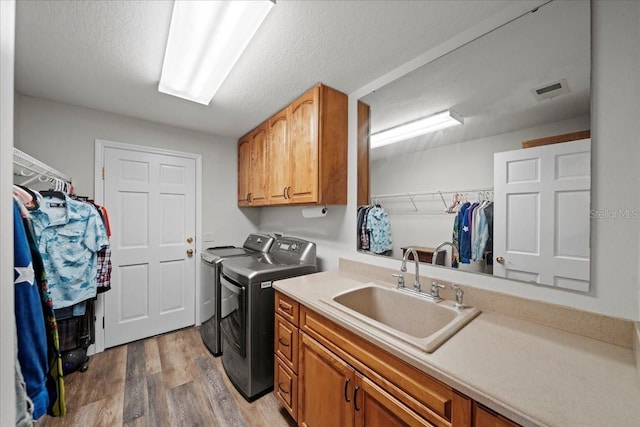 washroom with washing machine and clothes dryer, a sink, visible vents, light wood finished floors, and cabinet space