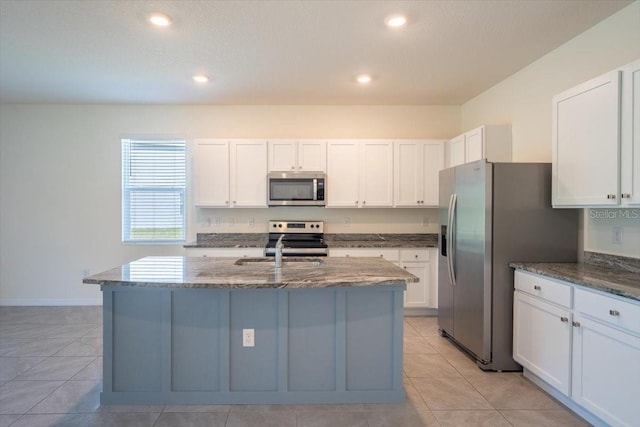 kitchen featuring light tile patterned floors, appliances with stainless steel finishes, dark stone countertops, and white cabinetry