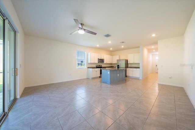 kitchen with a kitchen island with sink, dark countertops, appliances with stainless steel finishes, white cabinets, and open floor plan