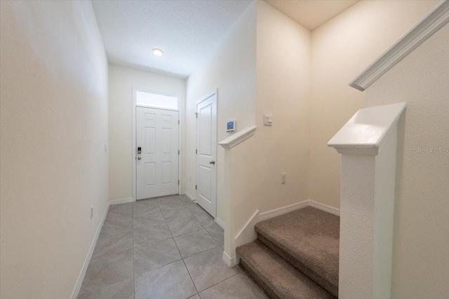 foyer featuring baseboards, light tile patterned floors, and stairway