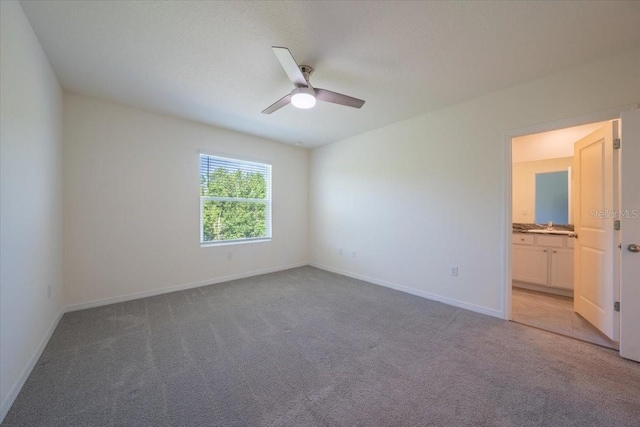 unfurnished room with a sink, baseboards, light carpet, and a ceiling fan