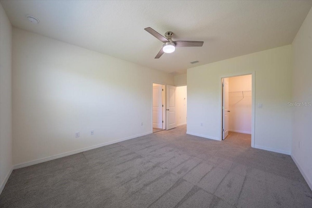 unfurnished bedroom with ceiling fan, a walk in closet, carpet, baseboards, and visible vents