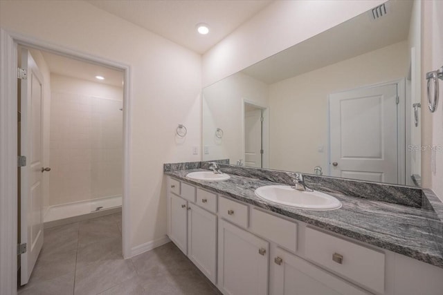bathroom with a sink, tile patterned flooring, double vanity, visible vents, and tiled shower
