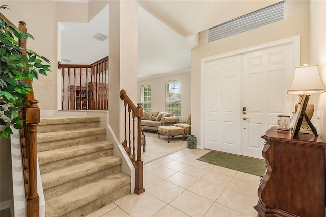 entrance foyer featuring light colored carpet, visible vents, baseboards, stairs, and light tile patterned flooring
