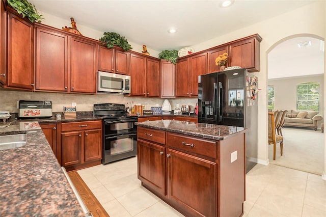 kitchen with visible vents, arched walkways, dark stone countertops, light tile patterned floors, and black appliances
