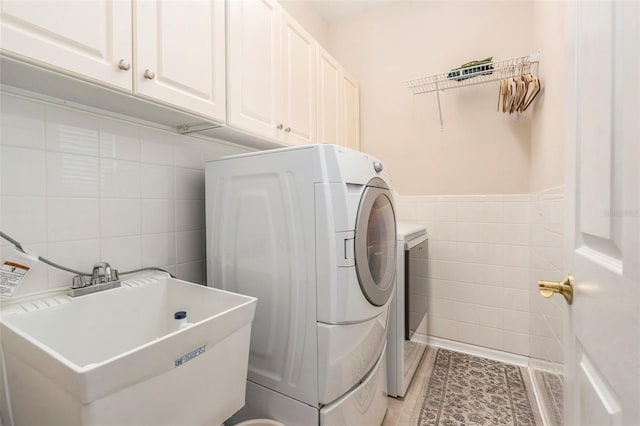 clothes washing area with a sink, cabinet space, independent washer and dryer, and tile walls