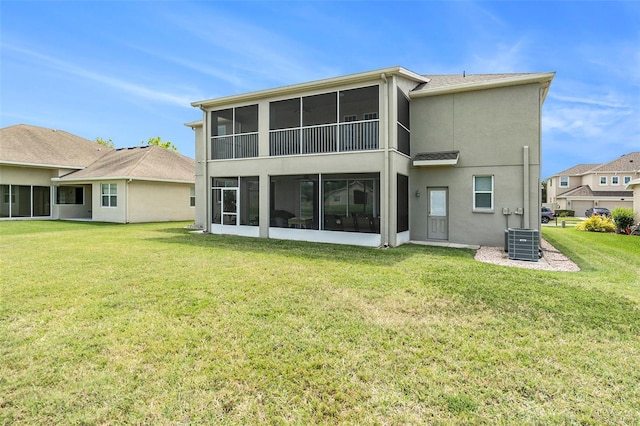 rear view of house featuring a lawn, central air condition unit, stucco siding, and a sunroom
