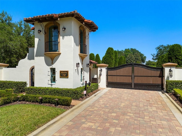 view of side of home with a gate, stucco siding, a balcony, and a tile roof