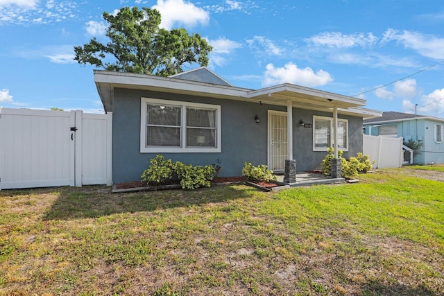 bungalow-style house featuring fence, a front lawn, and stucco siding