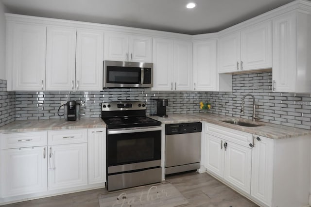 kitchen with tasteful backsplash, light stone countertops, appliances with stainless steel finishes, white cabinets, and a sink