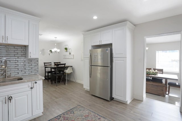 kitchen featuring tasteful backsplash, freestanding refrigerator, white cabinets, a sink, and baseboards