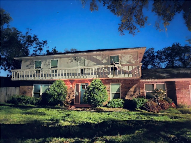 view of front facade featuring a balcony, a front lawn, and brick siding