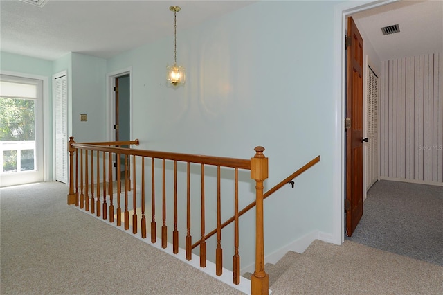 hallway with visible vents, baseboards, an upstairs landing, and carpet