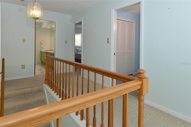 hall with a sink, carpet floors, baseboards, an upstairs landing, and an inviting chandelier