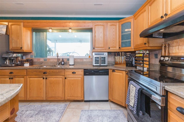 kitchen featuring light stone countertops, under cabinet range hood, tasteful backsplash, a sink, and appliances with stainless steel finishes