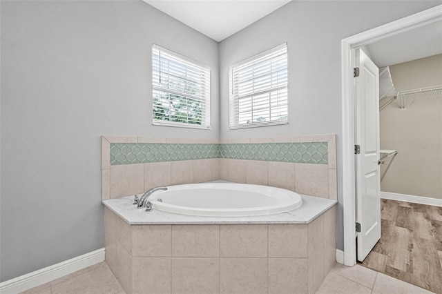 full bathroom featuring baseboards, tile patterned flooring, a walk in closet, and a garden tub